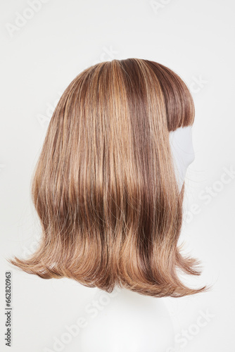 Natural looking dark brunet wig on white mannequin head. Middle length brown hair on the plastic wig holder isolated on white background, side view.