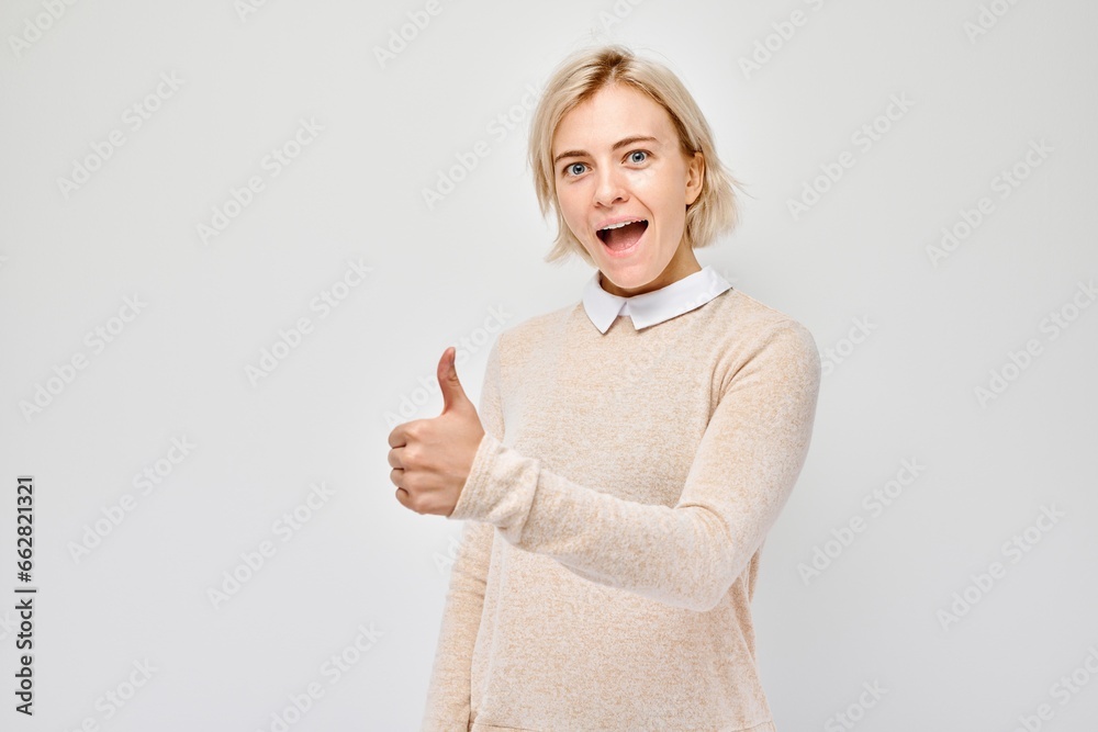 Portrait of young blond woman in casual clothing smiling joyfully showing thumbs up gesture isolated on white studio background. Approves good choice, right decision. Portrait of young blond woman in casual clothing smiling joyfully showing thumbs up gesture isolated on white studio background. Approves good choice, right decision.