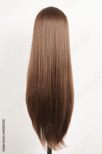 Natural looking dark brunet wig on white mannequin head. Long brown hair on the plastic wig holder isolated on white background, back view.