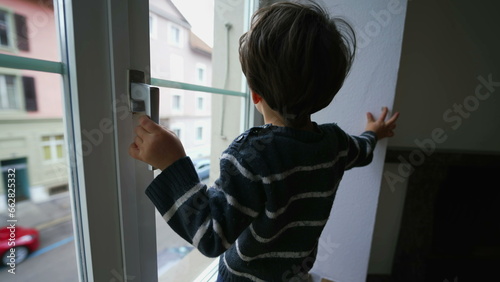 Child holding into window knob. Danger concept of small boy near glass from second floor apartment residence