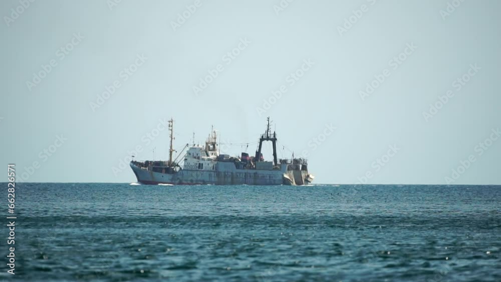 Fishing boat trawler catches fish while sailing on sea. A commercial fishing boat on the horizon in a distance sail to catch school of fish on calm sea surface in summer. Commercial catch of sea fish.