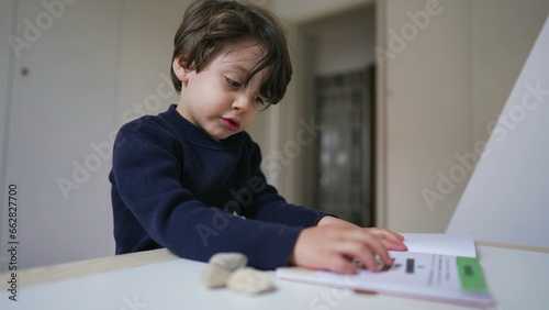 Wallpaper Mural Small boy reading book sitting at desk in bedroom. Curious child studying by himself turning page and looking at text and images Torontodigital.ca