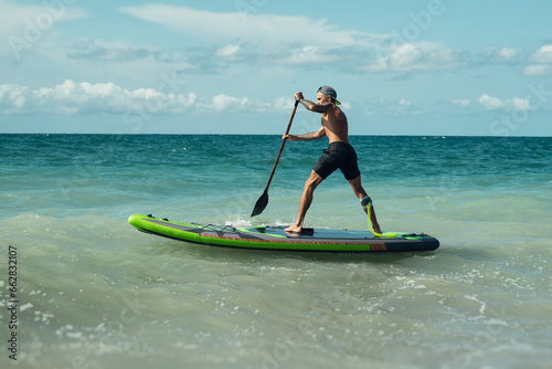 athletic wiry surfer guy swims with a paddle on a sup board in the sea © rotozey