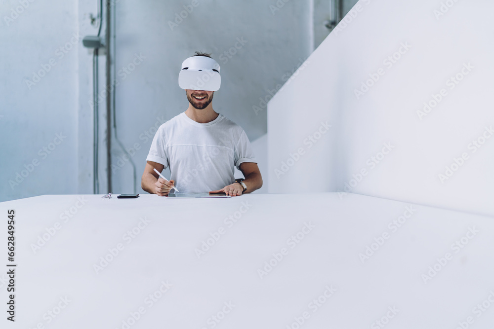 Smiling man sitting at table in virtual reality glasses Smiling man sitting at table in virtual reality glasses