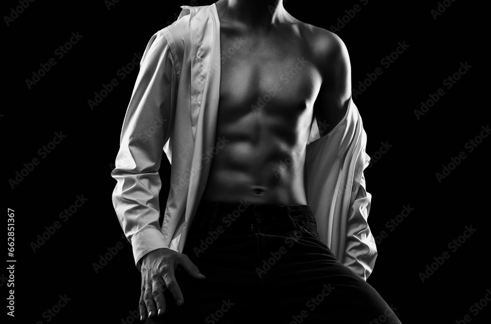 Fototapeta premium Handsome sexy man with a pumped up body in a dark shirt on a black background. Sports and healthy lifestyle.