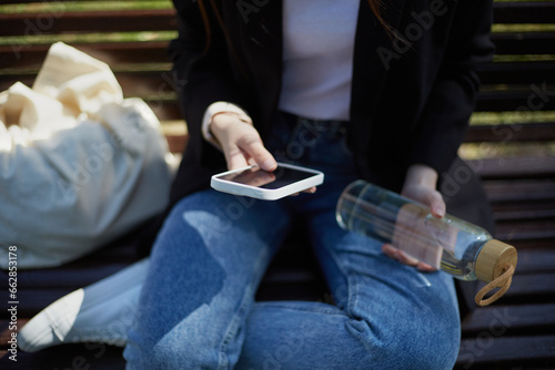 Young female chilling and browsing a smartphone on a bench