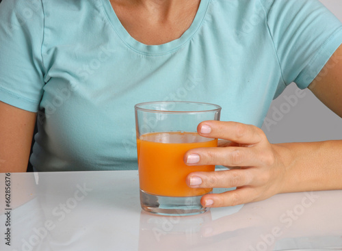 Woman hand hold oranje suice glass on kitchen table. photo
