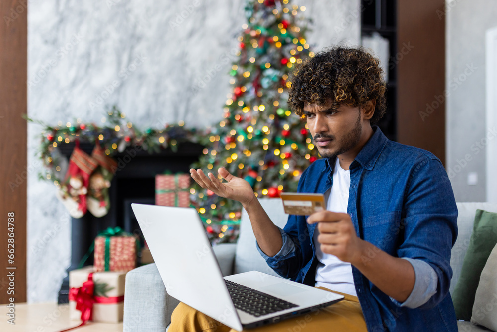 Upset cheated man lost money, refused to buy gift in online store, hispanic man using laptop and bank credit card for Christmas, upset and desperate, can't make money transfer. Upset cheated man lost money, refused to buy gift in online store, hispanic man using laptop and bank credit card for Christmas, upset and desperate, can't make money transfer.