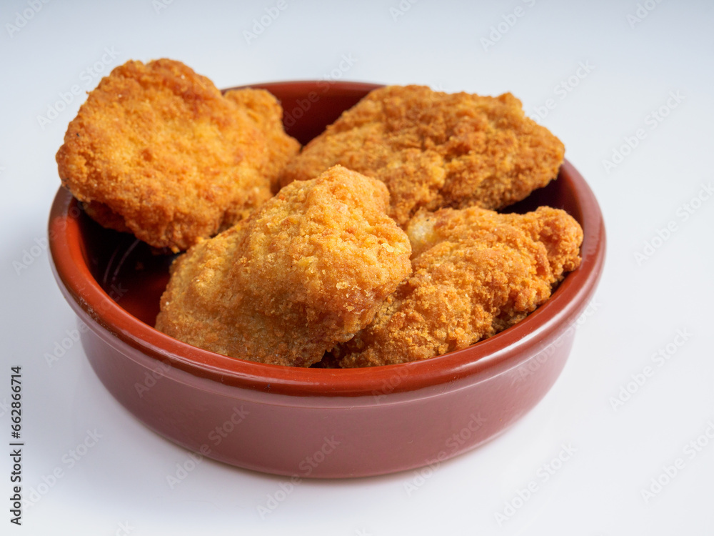 A round bowl of crispy fried chicken nuggets on a white background