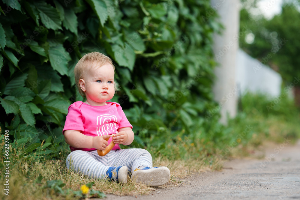 Portrait of a Caucasian blonde baby has a bagel on the background of a green bush with leaves