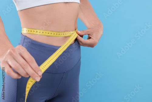 Slim woman measuring waist with tape on light blue background, closeup and space for text. Weight loss