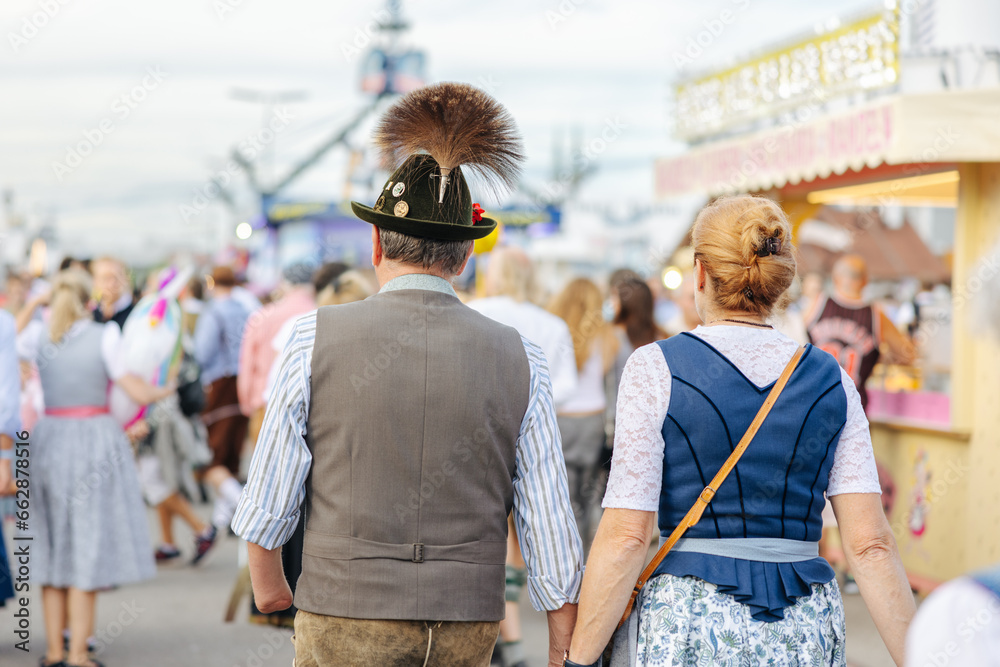 Fototapeta premium Man wearing Lederhosen and woman wearing the traditional Bavarian Dirndl at the Oktoberfest in Munich, Germany walking side by side close-up