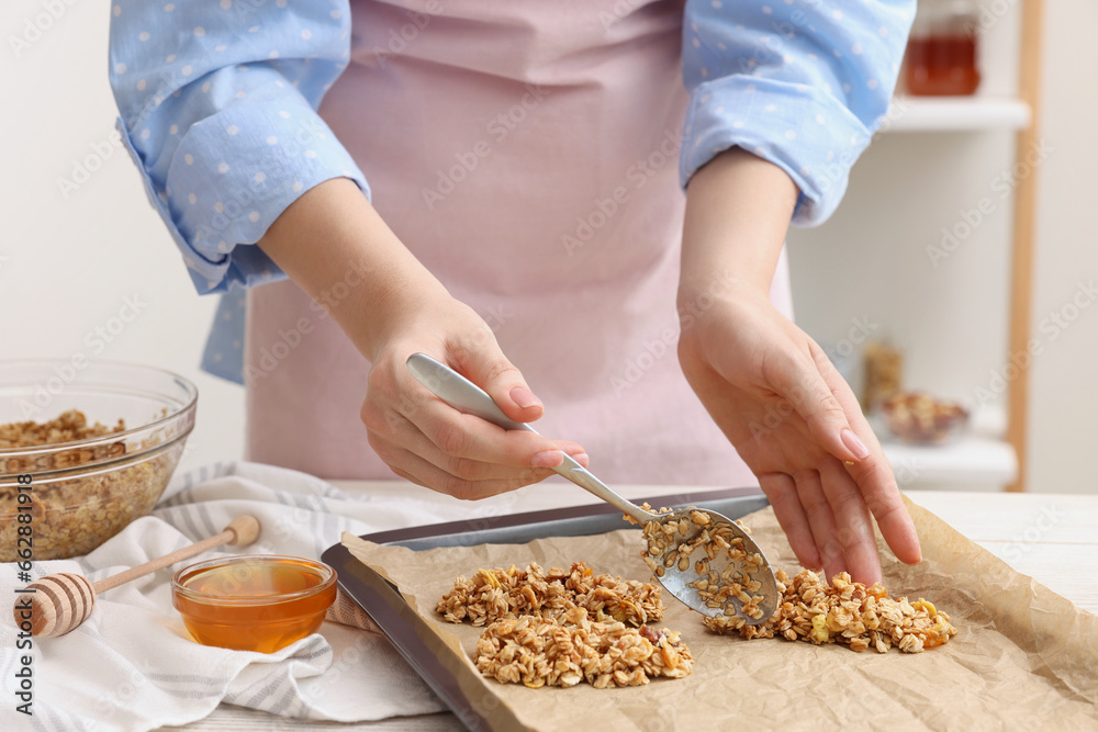 Making granola bars. Woman putting mixture of oat flakes, dry fruits and other ingredients onto baking tray at table in kitchen, closeup