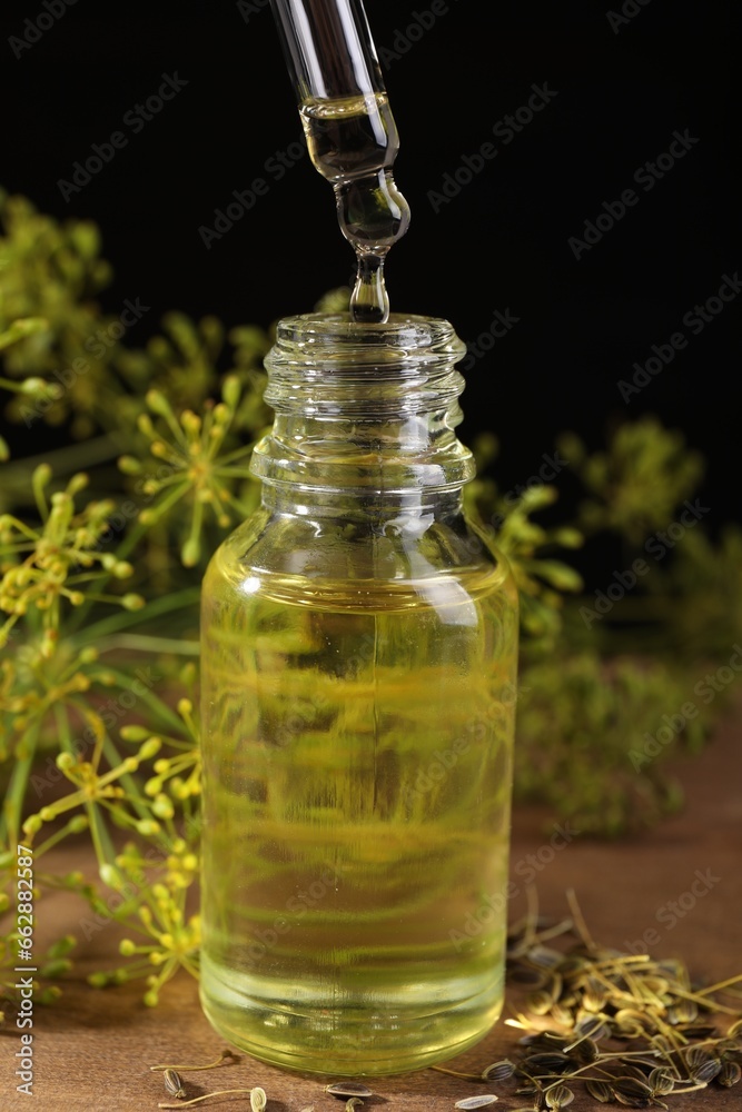 Dripping dill essential oil from pipette into bottle on wooden table, closeup Dripping dill essential oil from pipette into bottle on wooden table, closeup