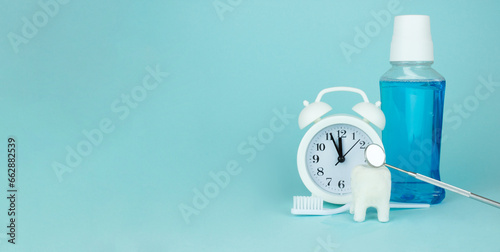 Care for oral and dental care concept. Regular checkups, oral health. Cropped view toothbrush, white tooth model, dentist mouth mirror, white analog alarm clock and Bottle Mouthwash on blue back.