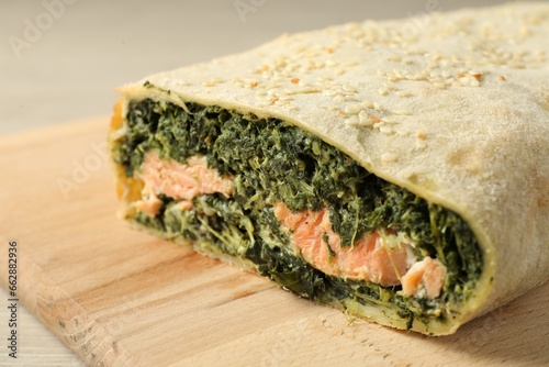 Delicious strudel with salmon and spinach served on light wooden table, closeup