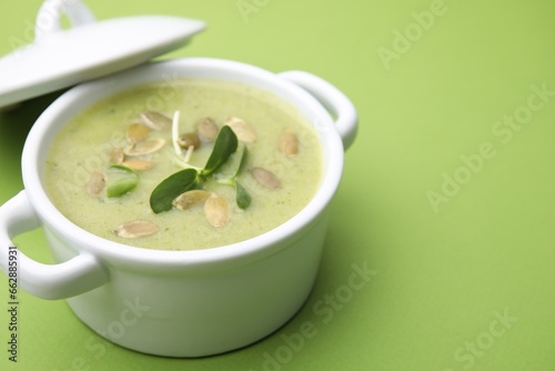 Delicious broccoli cream soup with pumpkin seeds on green background, closeup. Space for text