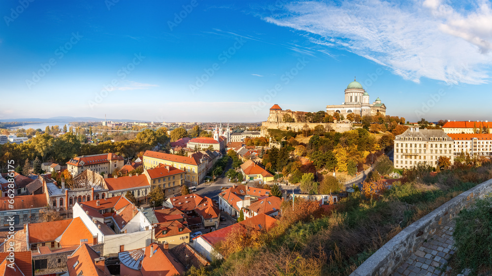 Seasonal autumnal panarama of Esztergom city, former capital of Hungary. Colorful onarnge-yellowish leafage of city parks beneath clear blu sky during sunny fall day. Landscape in natural colors.