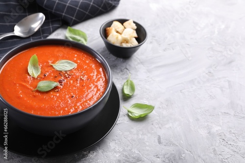 Delicious tomato cream soup served on grey textured table, closeup. Space for text