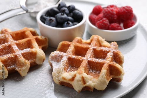 Delicious Belgian waffles with fresh berries and powdered sugar on plate, closeup