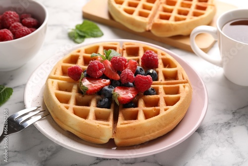 Tasty Belgian waffles with fresh berries served on white marble table, closeup