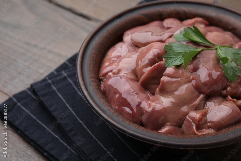 Bowl with raw chicken liver and parsley on wooden table, closeup. Space for text
