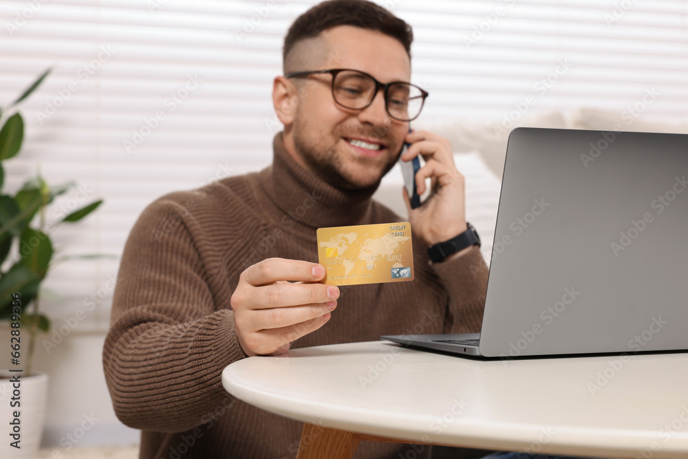 Handsome man with credit card using smartphone and laptop for online shopping at home, selective focus Handsome man with credit card using smartphone and laptop for online shopping at home, selective focus