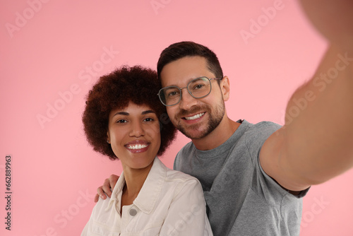 International dating. Happy couple taking selfie on pink background