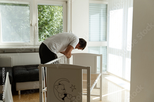 Young man assembling white wooden cot in nursery for expectant baby