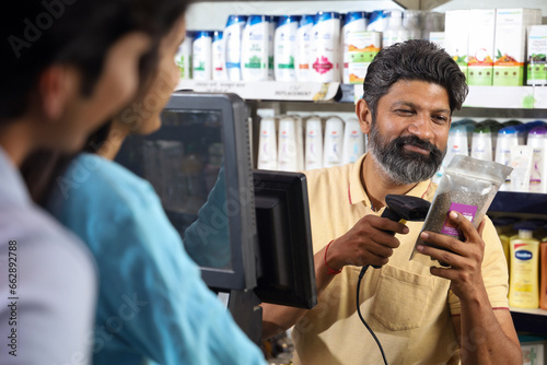 Bearded guy on the billing counter scanning the products. Customers standing in the queue in a mini shopping hyperstore. supermart. retail store. Bill