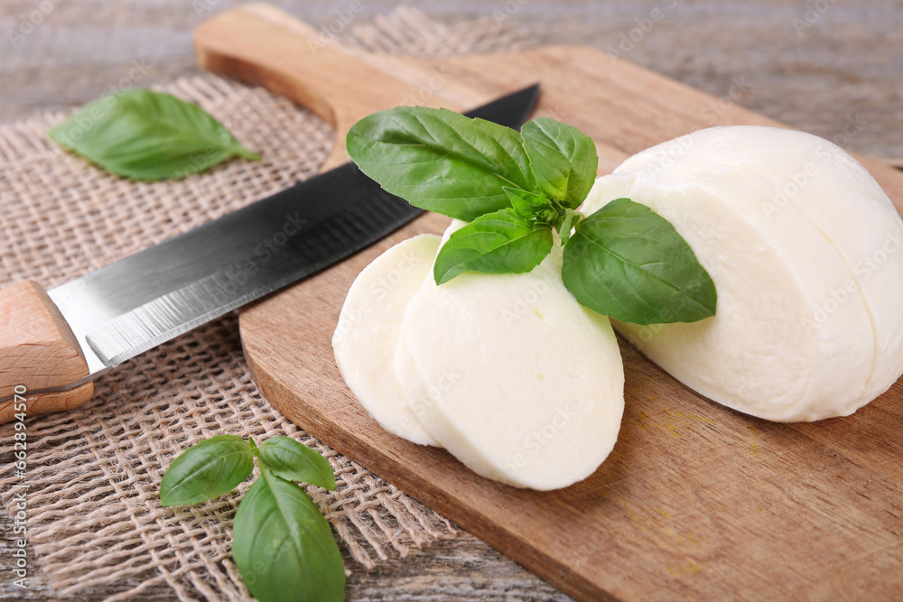 Slices of tasty mozzarella, basil leaves and knife on wooden table, closeup Slices of tasty mozzarella, basil leaves and knife on wooden table, closeup