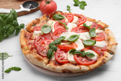 Delicious Caprese pizza with tomatoes, mozzarella and basil on white marble table, closeup