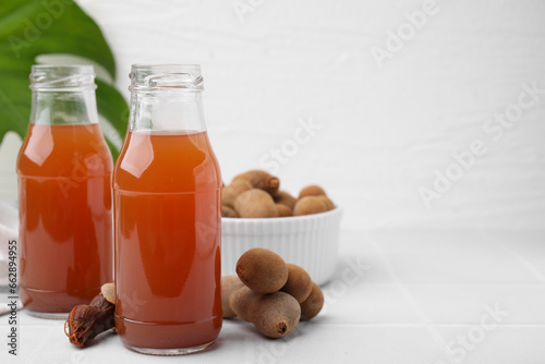 Tamarind juice and fresh fruits on white tiled table, space for text