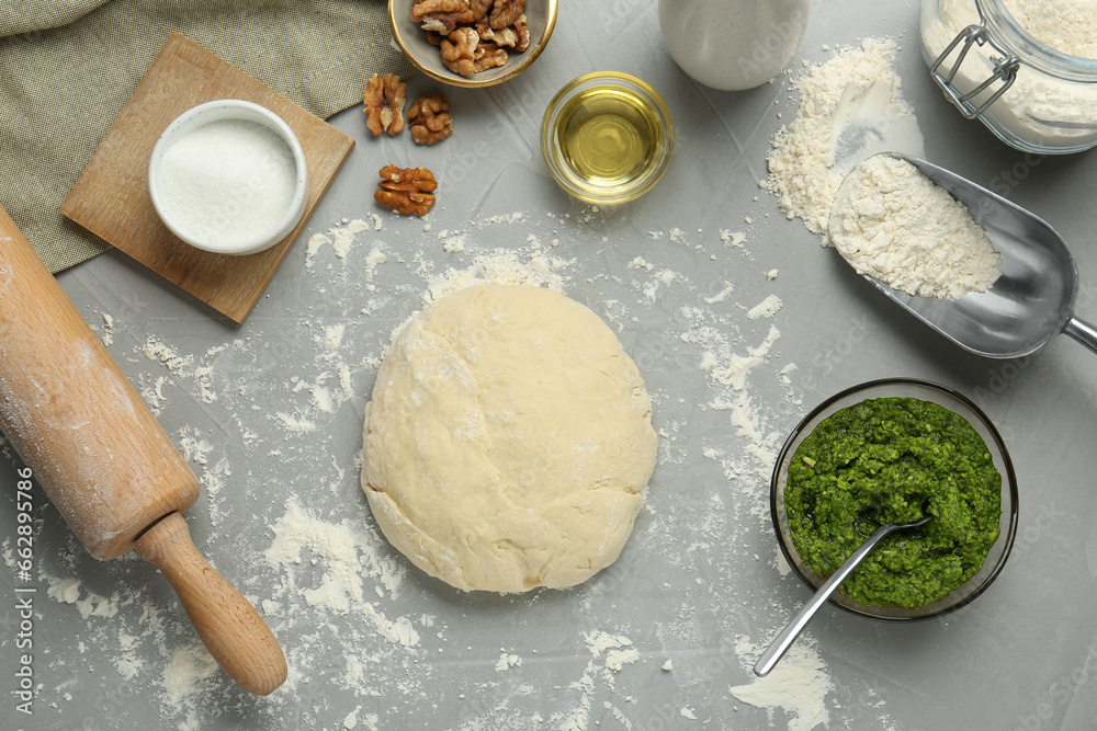 Fototapeta premium Making delicious pesto bread. Raw dough and ingredients on grey table, flat lay
