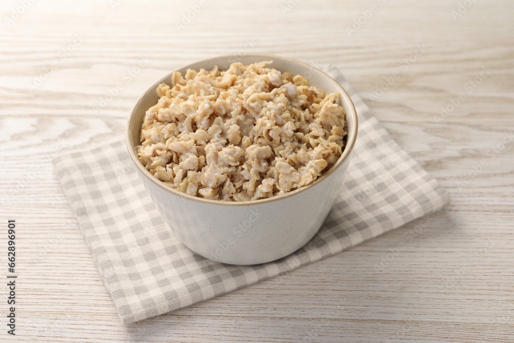 Tasty boiled oatmeal in bowl on light wooden table Tasty boiled oatmeal in bowl on light wooden table
