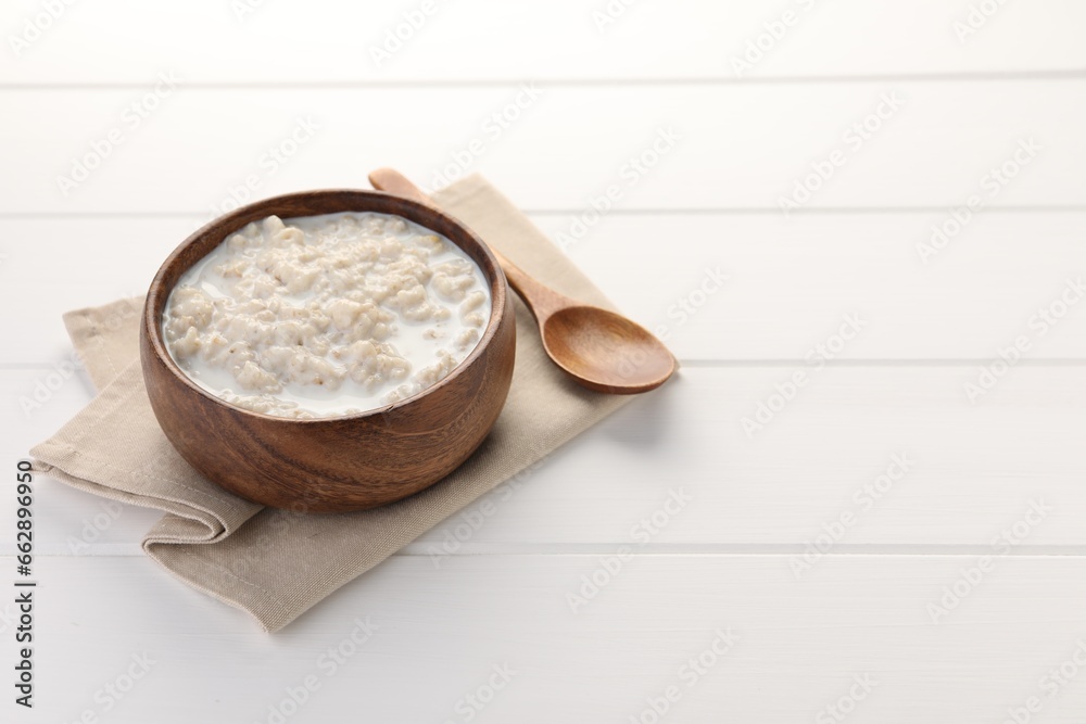 Tasty boiled oatmeal in bowl and spoon on white wooden table, space for text Tasty boiled oatmeal in bowl and spoon on white wooden table, space for text