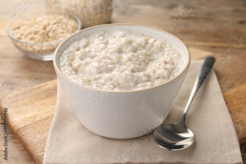 Tasty boiled oatmeal in bowl and spoon on wooden table, closeup