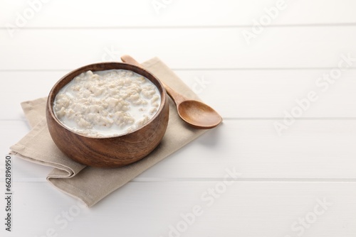 Tasty boiled oatmeal in bowl and spoon on white wooden table, space for text