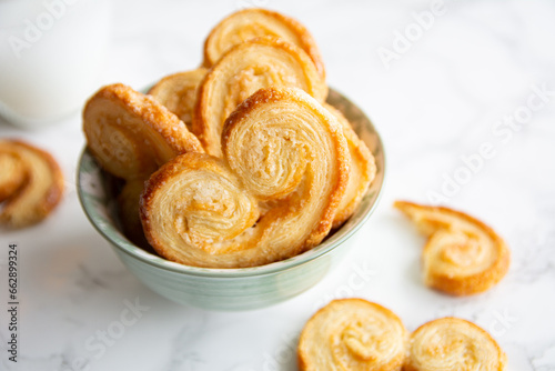 Puff pastry palmiers in a bowl on a white marble table. Homemade bakery.