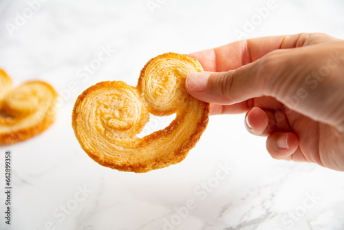 Young woman's hand holding a puff pastry palmier on a light background. Homemade bakery. photo