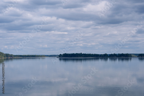 A peaceful, beautiful lake with calm water and a strip of forest visible in the distance on the other side. Harmony with nature