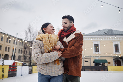 Waist up portrait of romantic young couple at outdoor ice skating rink looking at each other with love