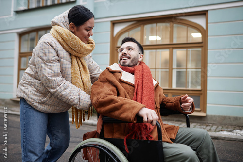 Bilde på lerret Portrait of smiling young woman assisting partner with disability outdoors in ci
