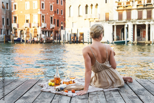 Lovely young woman picturesque picnic on the wooden gondola dock with rose wine, fruits and snack on wooden pier © blackday
