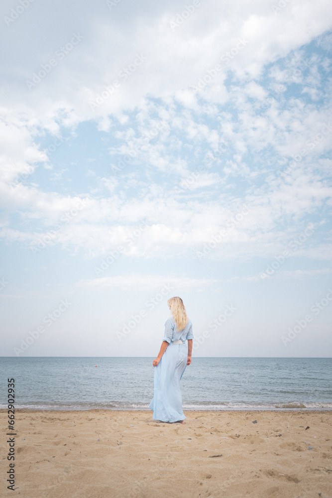 sea, sky, clouds, sunset, ocean, blonde woman in a floating dress stands with her back to the viewer, blue, without face, horizontal, photo sea, sky, clouds, sunset, ocean, blonde woman in a floating dress stands with her back to the viewer, blue, without face, horizontal, photo
