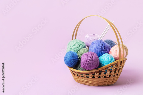 Lots of colorful knitting balls in a basket with knitting needles on a pastel purple background. Set for the hobby of knitting warm clothes or toys. Concept needlework