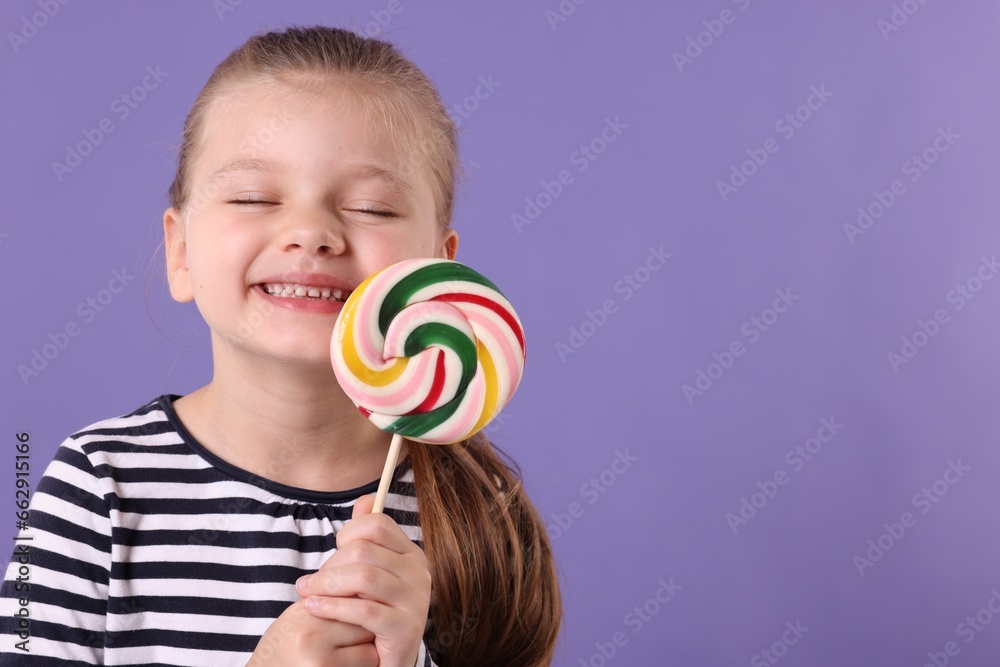 Happy little girl with colorful lollipop swirl on violet background, space for text