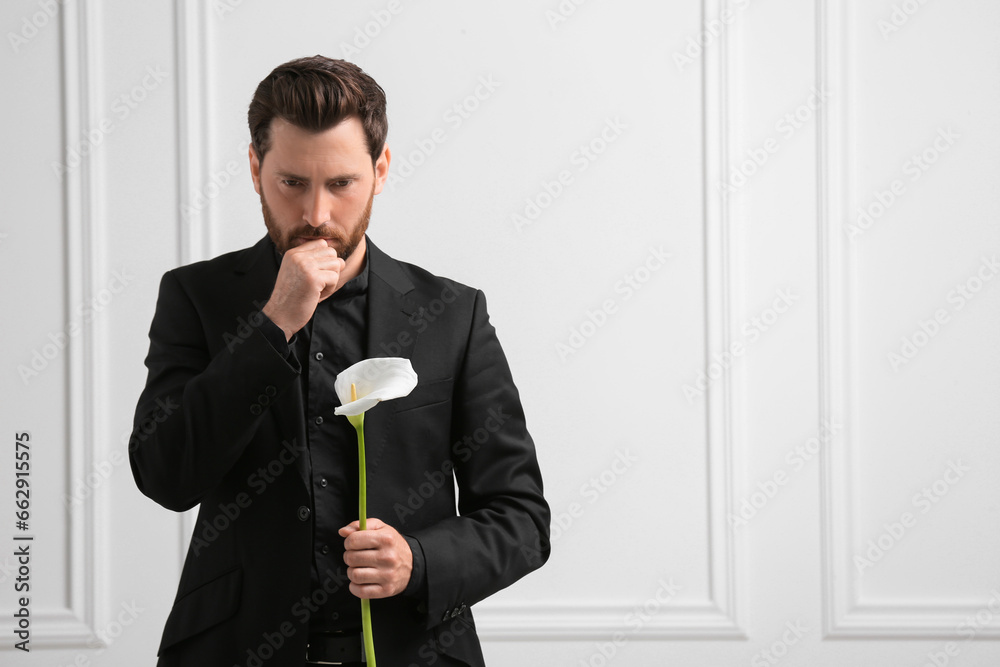 Sad man with calla lily flower near white wall, space for text. Funeral ceremony Sad man with calla lily flower near white wall, space for text. Funeral ceremony