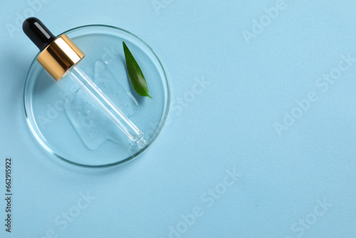 Petri dish with sample of cosmetic oil, pipette and green leaf on light blue background, top view. Space for text