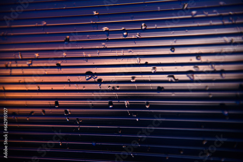 Blue-purple polycarbonate with raindrops. View of wet glass in the setting sun.
